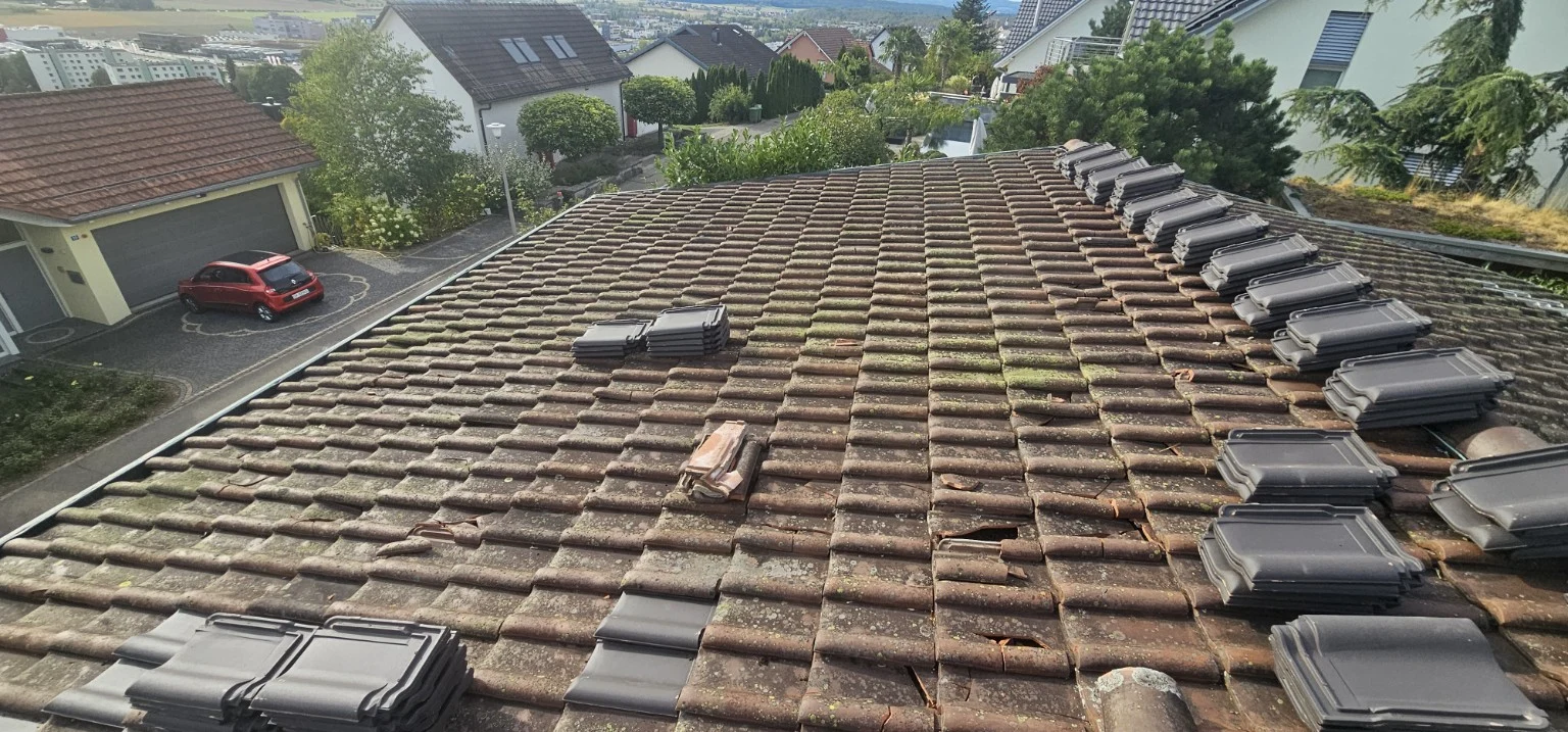Bereitgelegte Ersatzziegel auf dem Dach neben beschädigten Bereichen